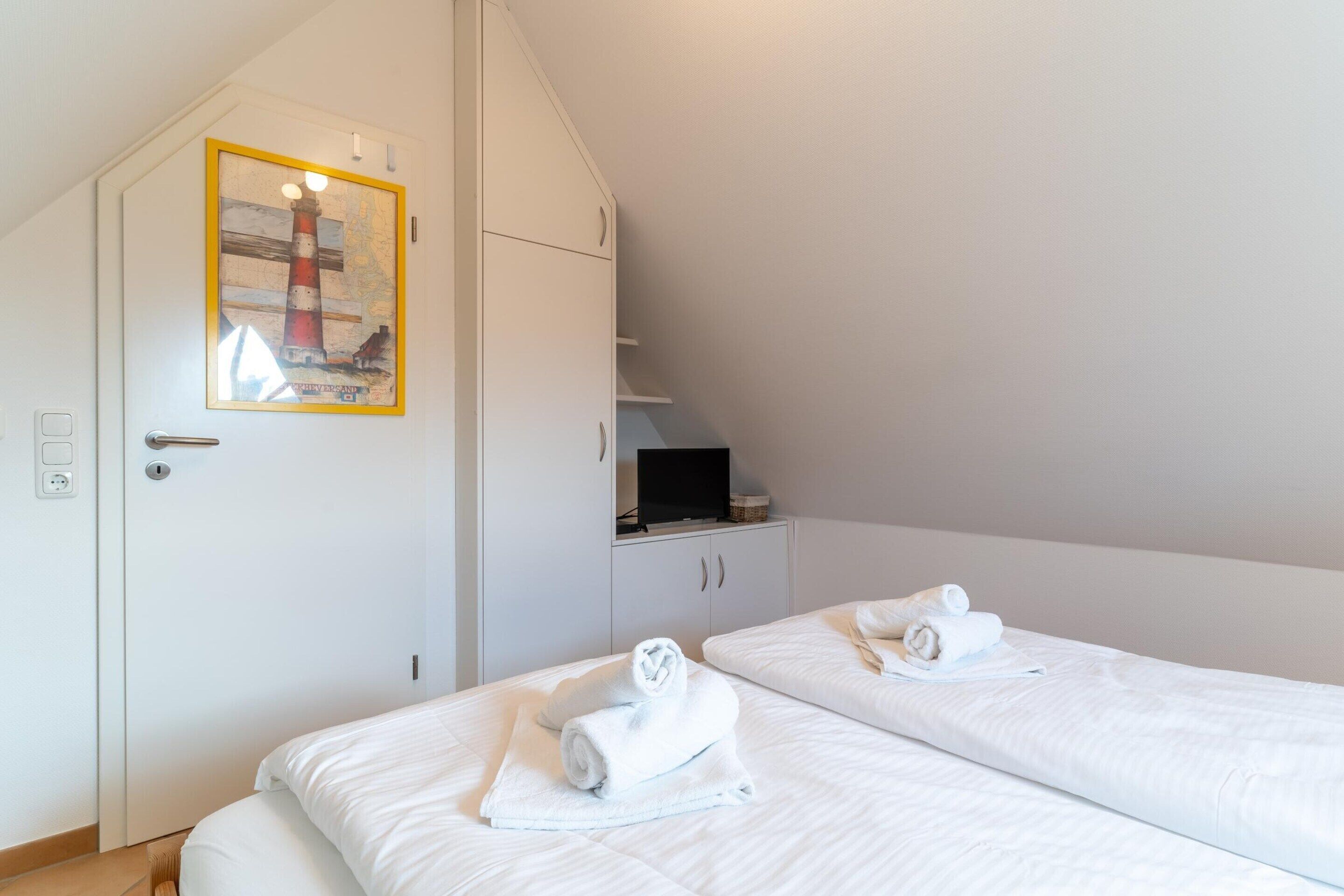 Et hotelværelse med to senge, et maleri af et fyrtårn, et fjernsyn og et lille skab.
