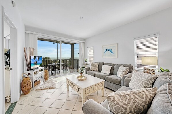 A spacious living room with a large TV, grey sofa, and a balcony with a view of the ocean. - Shell Island Beach Club 6B | Amazing Ocean/Gulf Front Beach Views Condo (Sanibel)
