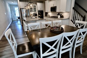 A modern kitchen with white cabinetry, a central island with seating, and a dining area with white chairs.