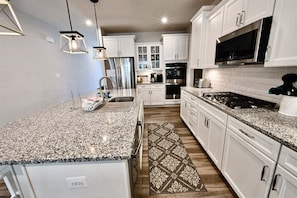 A kitchen with white cabinets, granite countertops, stainless steel appliances, and pendant lighting.