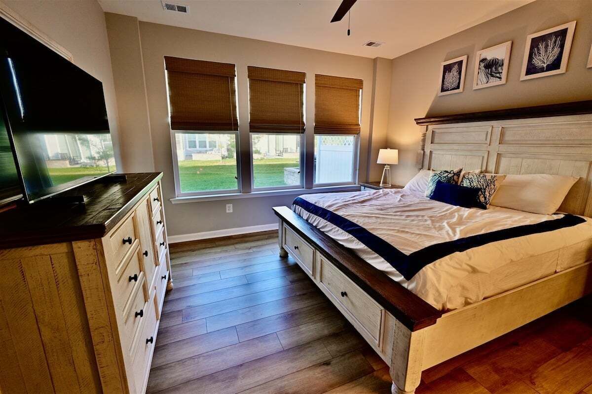 A bedroom with a bed, a TV, a dresser, and a window with blinds.