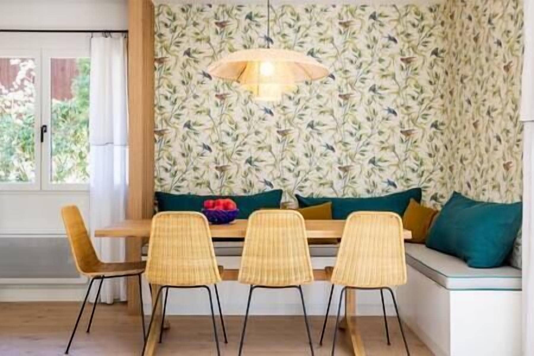 A dining area with a wooden table, three wicker chairs, and a bench with cushions.