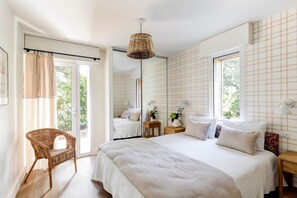 Une chambre à coucher avec un grand lit, une chaise en osier, des tables de chevet avec des lampes et un miroir.