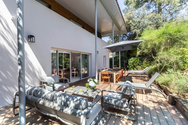 Un patio extérieur moderne doté d’une terrasse en bois, d’un canapé, d’une table à manger et d’un grand parasol.
