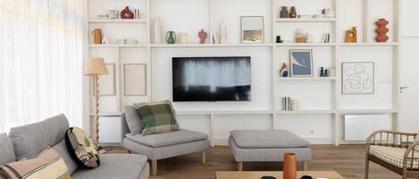 En moderne stue med en grå sofa, et træsofabord og et fjernsyn monteret på væggen.
