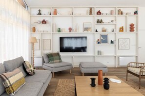 Ein modernes Wohnzimmer mit einem grauen Sofa, einem Holztisch und einem an der Wand befestigten Fernseher.