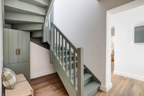 A staircase with a modern design, a wooden floor, and a view into a room with a cabinet and a cushion.