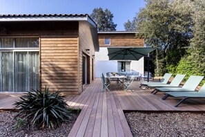 A wooden deck with a dining table and chairs, surrounded by lounge chairs and a large umbrella.