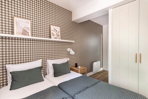 A bedroom with a checkered wall, a bed with white and dark green bedding, a bedside table with a lamp, and a wardrobe.