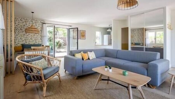 Ein Wohnzimmer mit blauem Sofa, Korbsessel, Holztisch und einer Pendelleuchte.