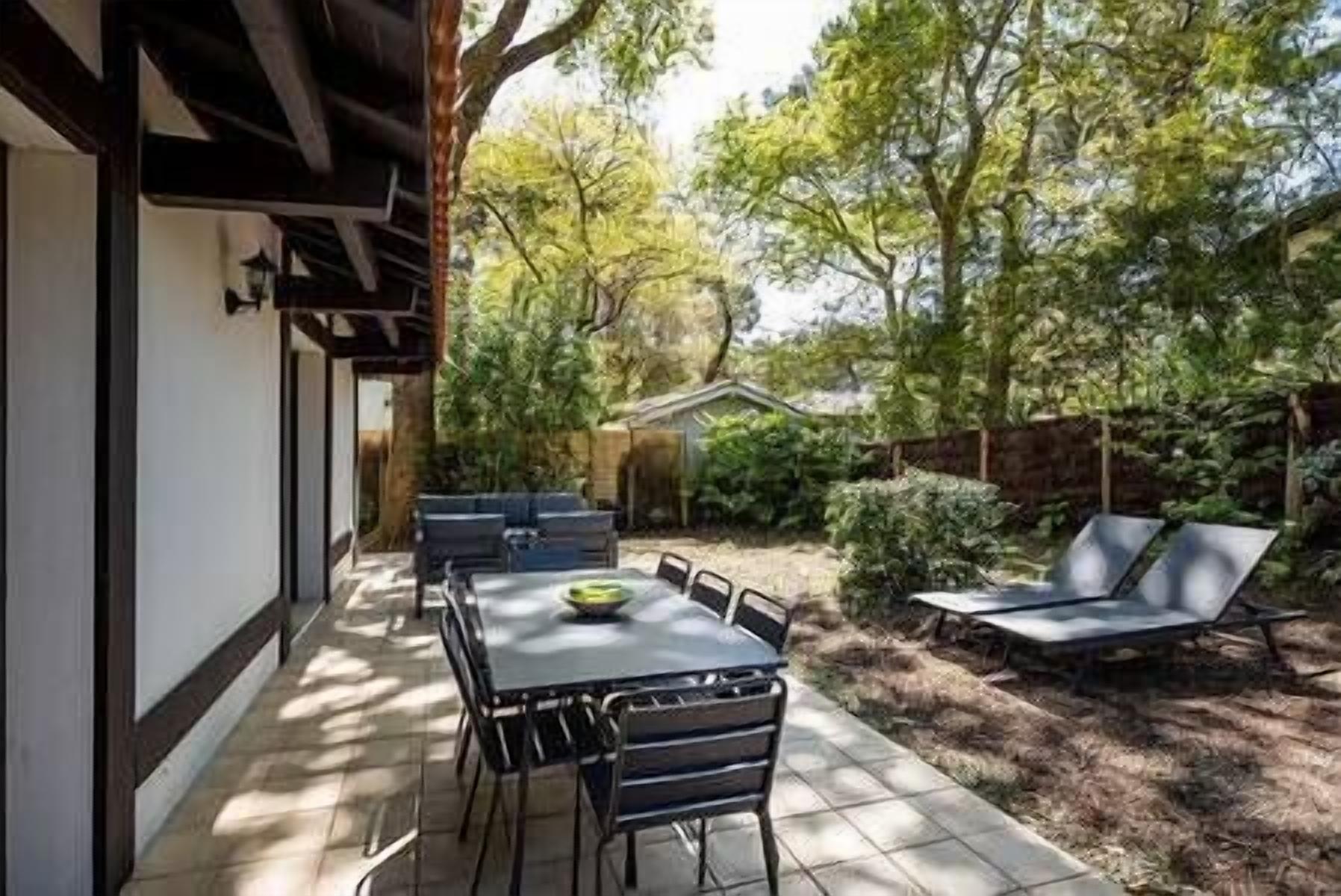 Une terrasse avec une table et des chaises, un fauteuil de relaxation et un petit abri de jardin, le tout aménagé dans un cadre verdoyant.