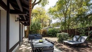 Eine Terrasse mit Tisch, Stühlen und einer Liege, sowie ein kleines Gartenhaus in einer Gartenanlage.