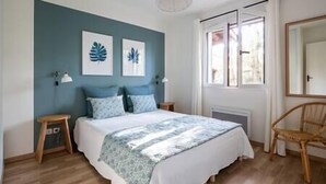 Een slaapkamer met een bed, twee nachtkastjes, een stoel en een raam met gordijnen.