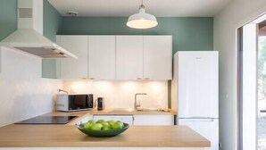 Een moderne keuken met witte kasten, een magnetron, een spoelbak en een schaal groene appels op het aanrecht.