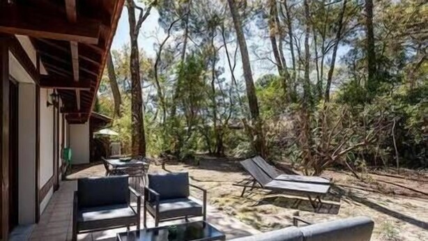 Een terras met een buitenbank, stoelen en een tafel, omringd door bomen en een houten terras.