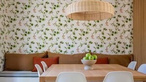 Een eetgedeelte met een houten tafel, witte stoelen, een schaal groene appels en bloemenbehang.