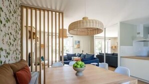 Een moderne woonkamer met een houten eettafel, witte stoelen, een blauwe bank en een decoratieve fruitschaal.
