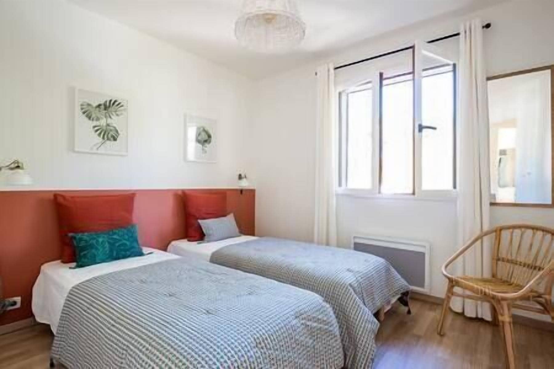 A room with two beds, a chair, and a window with curtains.