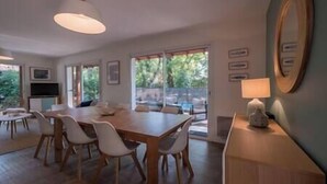 A dining area with a wooden table and chairs, a television, and a view of greenery outside.