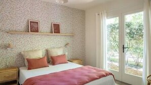 A bedroom with a bed, a nightstand, a dresser, and a window with a view of greenery.