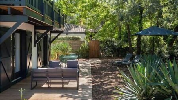 A patio area with a wooden deck, outdoor seating, and lush greenery.