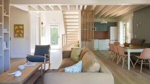A spacious living area with a sofa, chairs, a dining table, and a kitchen in the background.
