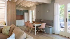 A modern living room with a sofa, dining table, and chairs. There is a kitchen area with cabinets and a refrigerator.