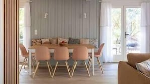 A dining area with a wooden table and four chairs, a sofa, and a view of the outdoors through a glass door.