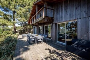 Una cabaña de madera con terraza, mobiliario exterior y ventanas amplias.