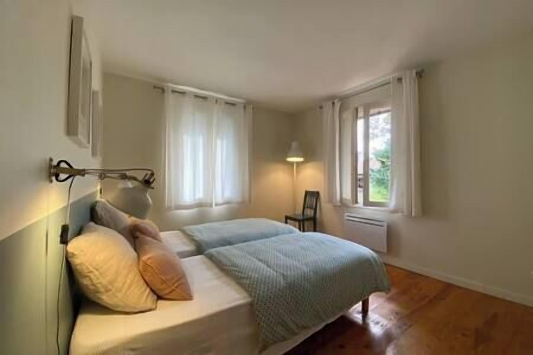 A bedroom with a bed, pillows, a chair, and a window.