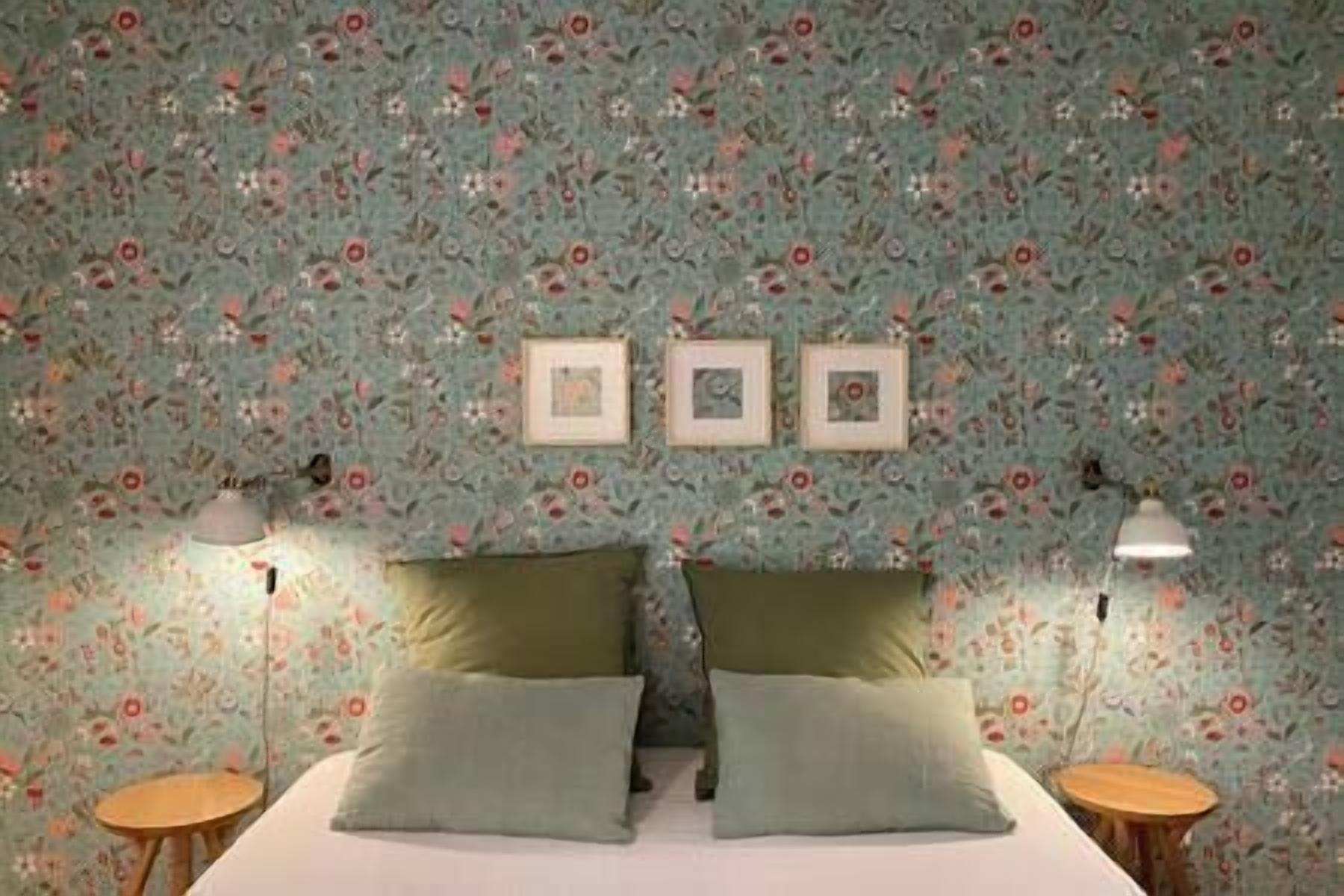 Ein Schlafzimmer mit blumigem Wandpapier, einem Bett mit zwei Kissen und drei gerahmten Bildern an der Wand.