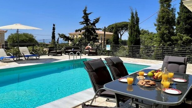 Zona junto a la piscina con una mesa lista para el desayuno, sillones de descanso y vista despejada a la piscina.