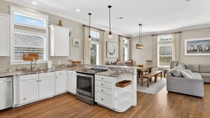 A modern kitchen with white cabinetry, a built-in oven, and a dining area with a wooden table and chairs. - Coastal Vue - Private Pool, Family Friendly, Gated & Private Community Beach. (Seacrest)