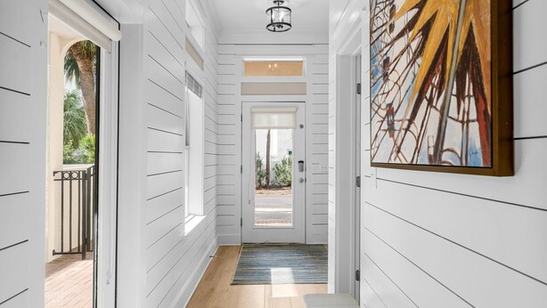 A hallway with white paneling, a door leading outside, and a painting on the wall. - Coastal Vue - Private Pool, Family Friendly, Gated & Private Community Beach. (Seacrest)
