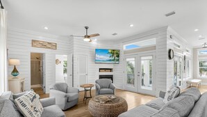 A spacious living room with a fireplace, grey sofas, a television, and a large window overlooking a balcony. - Coastal Vue - Private Pool, Family Friendly, Gated & Private Community Beach. (Seacrest)