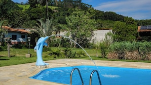 Una piscina con elemento d'acqua, circondata da un solarium in pietra e rigogliosa vegetazione.