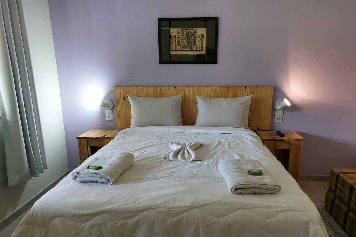 Ett hotellrum med en stor säng, två sängbord, en inramad tavla på väggen och ett fönster med gardiner.