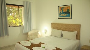 Una camera d'hotel con un letto grande, una testiera, un comodino, una sedia, una finestra con tende e un quadro appeso al muro.