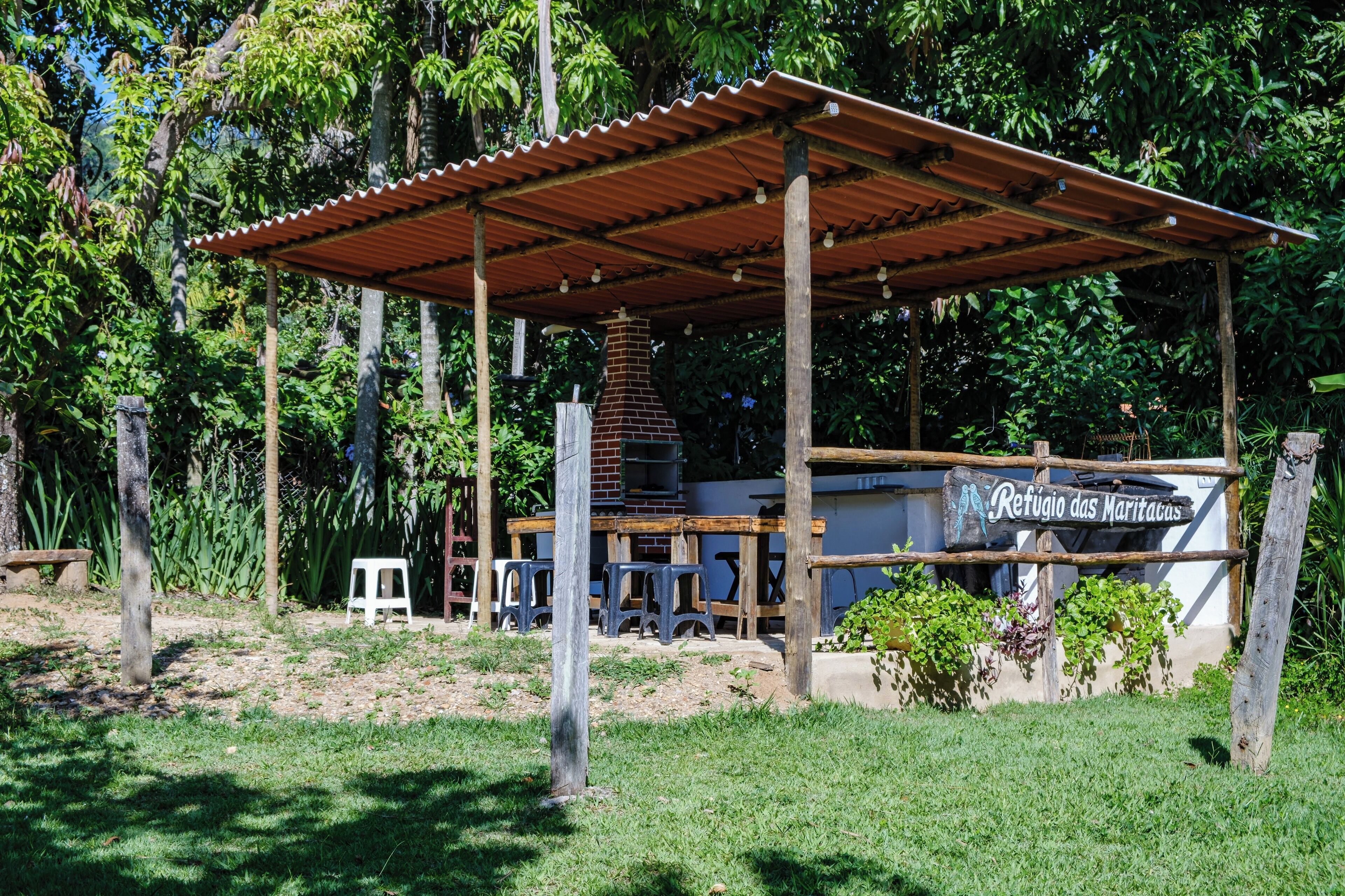 Un espacio al aire libre rústico con terraza cubierta, mesas de madera y chimenea de ladrillo.