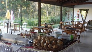 Un ristorante con posti a sedere all'aperto, tavoli, sedie e un'area buffet con pane e condimenti.