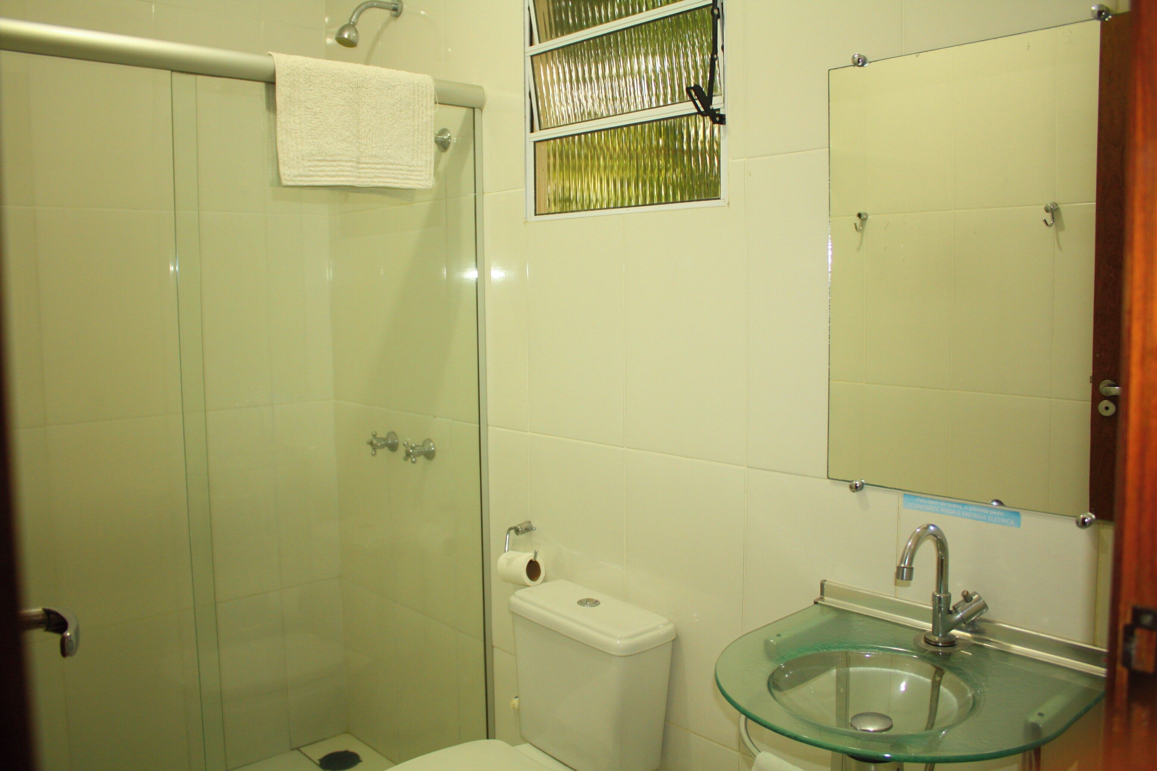 A bathroom with a glass shower enclosure, a toilet, a glass sink, and a mirror.