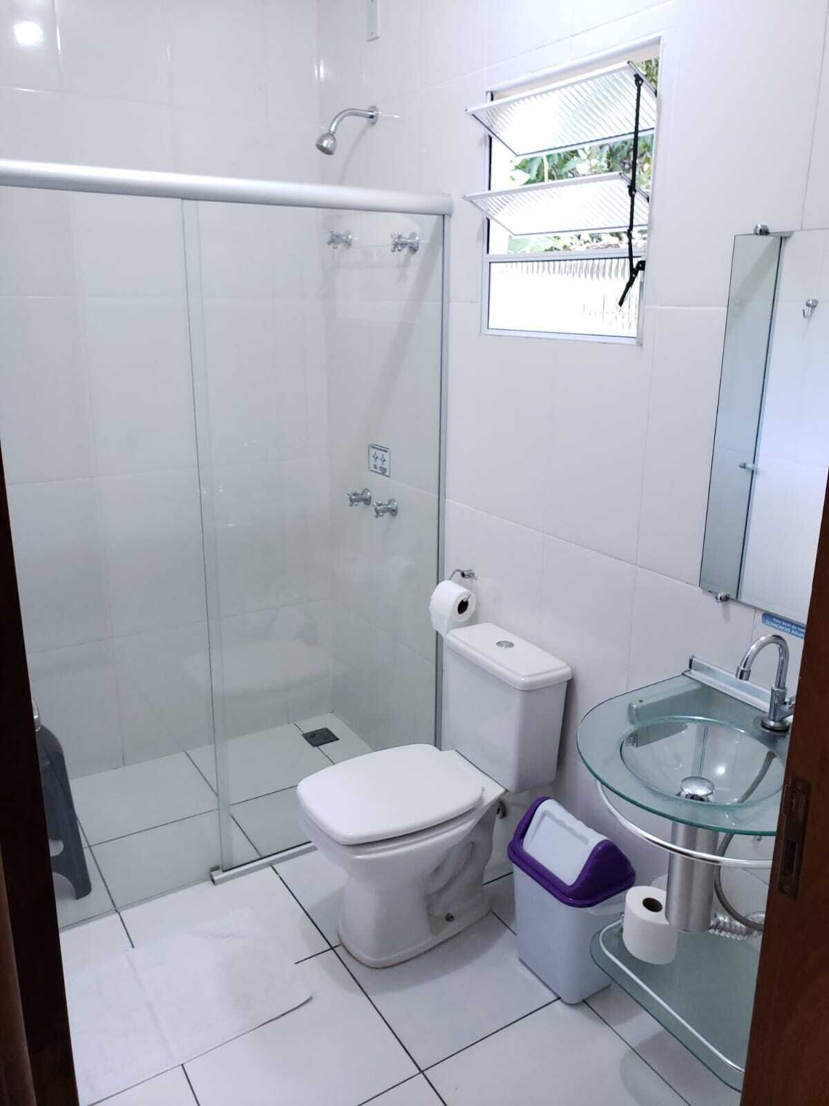Een moderne badkamer met een douchecabine van glas, een wit toilet, een glazen wastafel en een klein spiegel boven de wastafel.