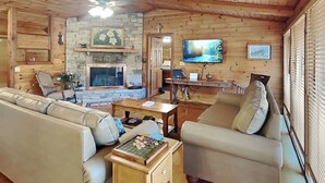 A cozy living room with a stone fireplace, wooden walls, a television, and comfortable seating. - Alexander's Lookout by Jackson Mountain Rentals (Gatlinburg)