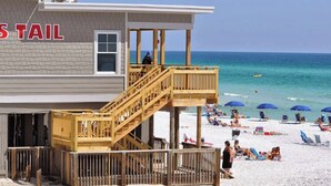Un bâtiment situé en bord de mer, doté d’une terrasse en bois et d’un escalier menant à un balcon.