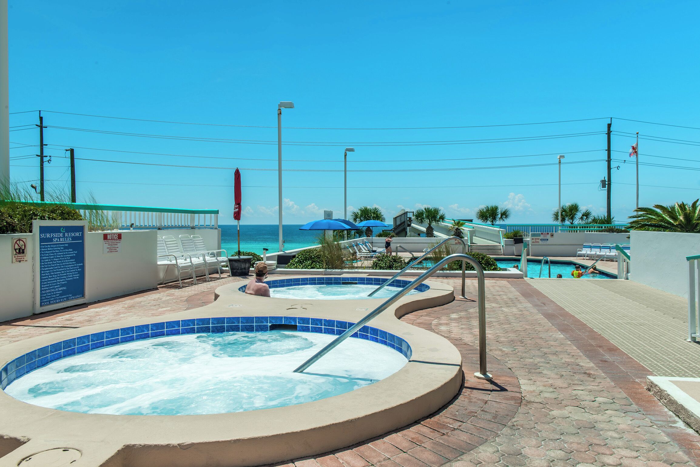 A pool area with hot tubs and lounge chairs, a pool, and a view of the ocean.