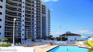 Um hotel com piscina, espreguiçadeiras e um edifício grande com varandas.