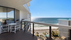 Varanda com vista para o oceano, mobiliada com cadeiras e mesa brancas.