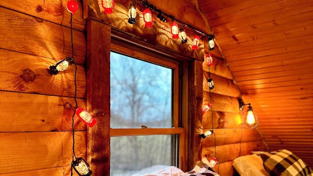 Una habitación de cabaña acogedora con interior de madera, una cama a cuadros y luces colgantes.