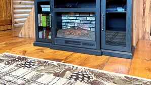 Un interior de madera con una chimenea, un televisor de pantalla plana montado encima y una alfombra estampada en el suelo.