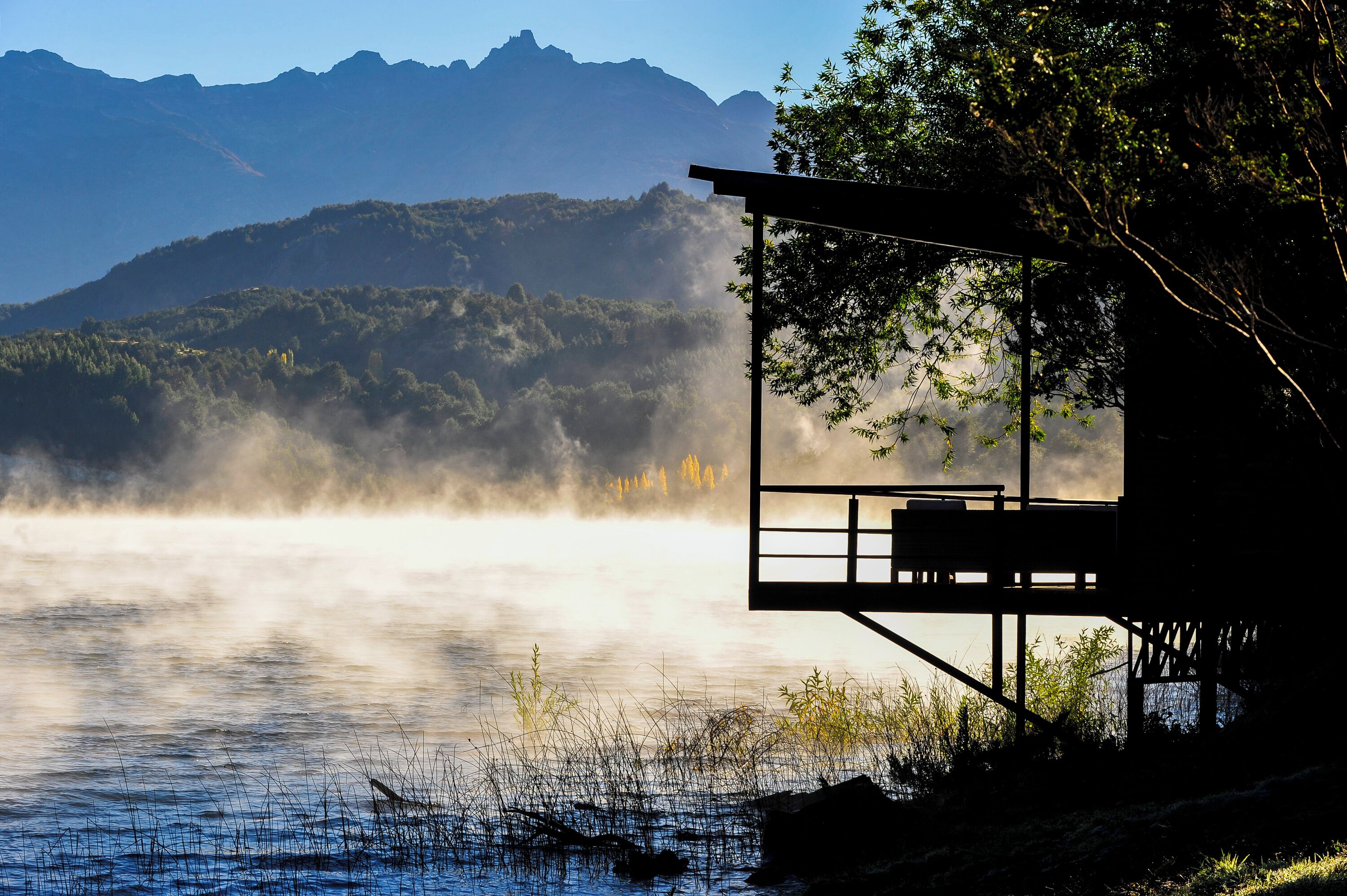 Una cabaña junto al lago con vistas a montañas envueltas en niebla.